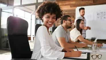 Persona sorridente seduta a un tavolo in un ufficio moderno.