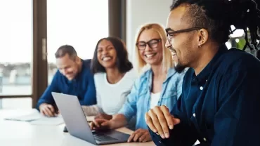 Persone sorridenti in riunione intorno a un tavolo.
