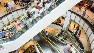 Centro commerciale affollato con scale mobili in movimento.