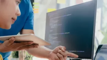 Persona che lavora al computer con codice sullo schermo.