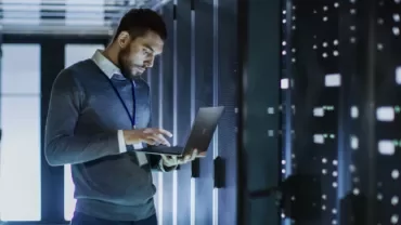 Persona controlla i dati su un laptop in una stanza server.