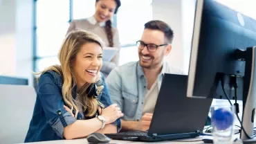 Persone che ridono e lavorano insieme al computer in un ufficio.