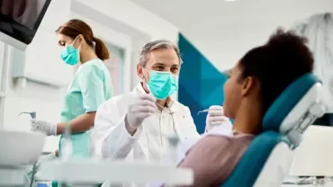 Dentista con maschera e paziente in studio odontoiatrico.