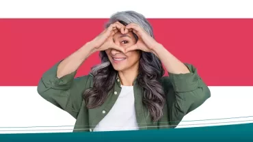 Persona sorridente con le mani a forma di cuore sul viso.