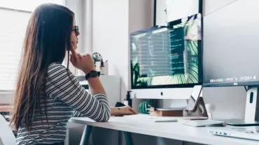 Persona al computer in ufficio moderno con schermo ampio.