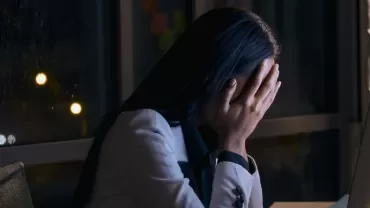 Persona davanti al computer con mani sul viso in un ufficio di notte.