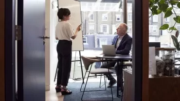 Persona parla davanti a una lavagna in un ufficio con una finestra grande.