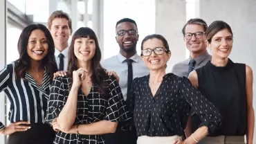 Gruppo eterogeneo di adulti in abbigliamento professionale che sorridono in un contesto d’ufficio.