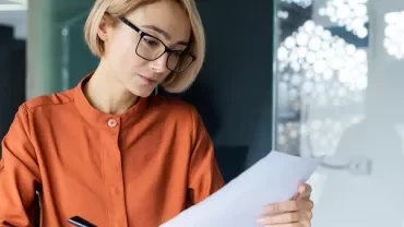 Donna bionda con occhiali che legge un foglio di carta