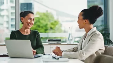 Due professioniste discutono ad un tavolo, di fronte ad un laptop