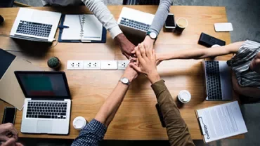 Persone riunite intorno a un tavolo con computer portatili.