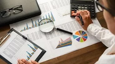 Persona al lavoro con grafici e calcolatrice su una scrivania.