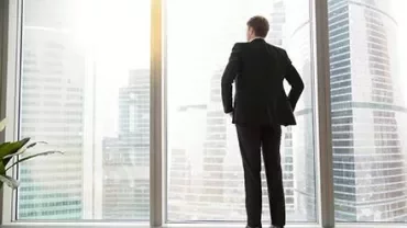 Persona in abito guarda fuori dalla finestra di un grattacielo.