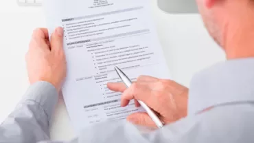 Persona che revisiona un curriculum su un tavolo bianco.