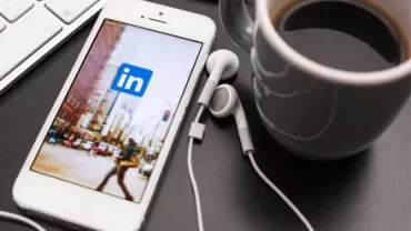 Smartphone con app LinkedIn aperta su scrivania accanto a tazza di caffè.