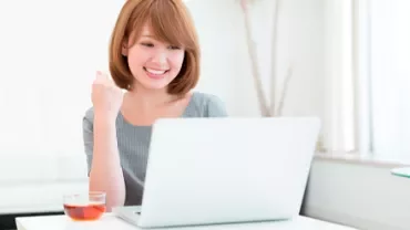 Persona sorridente davanti a un laptop con una tazza di tè sul tavolo.