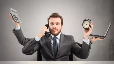 Persona multitasking con telefono, sveglia, calcolatrice e laptop.