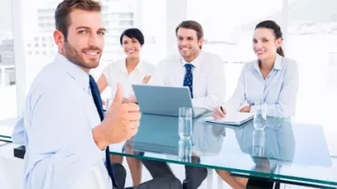 Persone in riunione sorridono intorno a un tavolo di vetro.