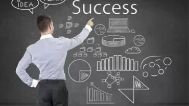 Persona davanti a una lavagna con disegni di grafici e la parola 'Success'.