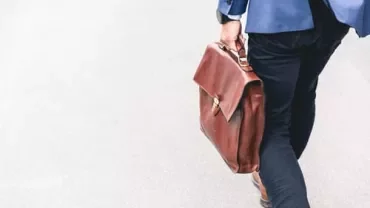 Persona che cammina con una borsa di pelle marrone.