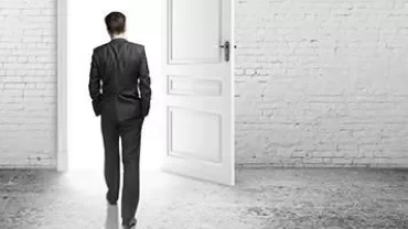 Persona in abito si allontana verso una porta aperta, luce intensa all'esterno.