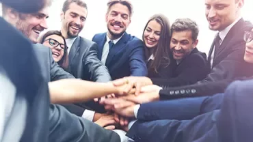 Gruppo di persone in abiti formali che si danno la mano in cerchio.
