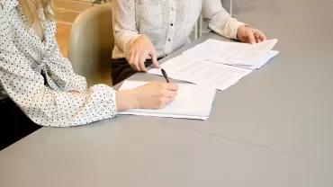 Due persone discutono documenti a un tavolo.