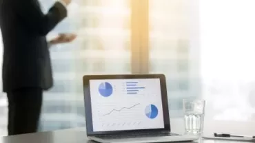 Ufficio moderno con laptop e grafici su schermo.