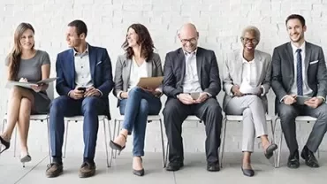 Gruppo di persone sedute in attesa, indossano abiti formali.