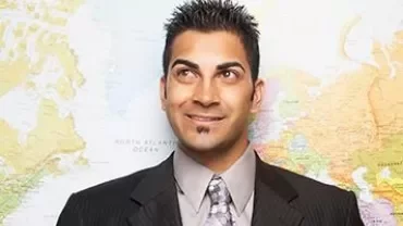 Persona in abito formale davanti a una mappa geografica.
