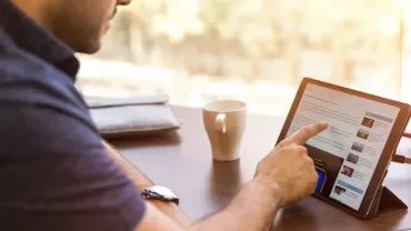Persona che usa un tablet al tavolo con tazza di caffè.
