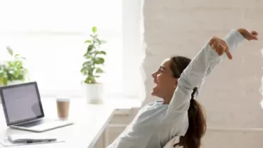 Persona felice si allunga alla scrivania accanto a un laptop.