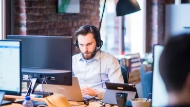Persona al lavoro con cuffie e computer in un ufficio moderno.