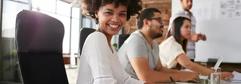 Persona sorridente seduta a un tavolo in un ufficio moderno.
