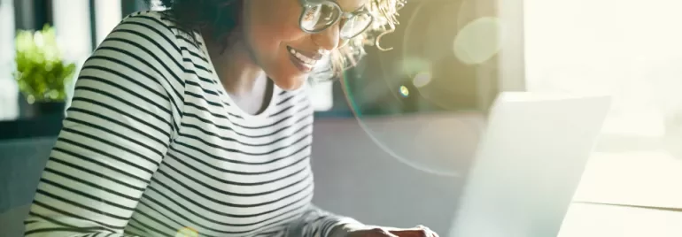 Persona sorridente che utilizza un laptop, con luce solare che entra dalla finestra.