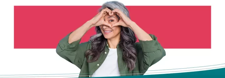 Persona sorridente con le mani a forma di cuore sul viso.