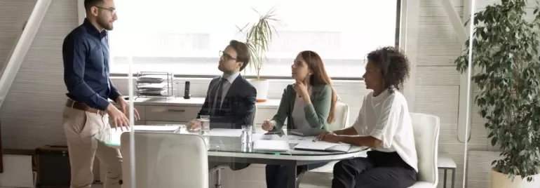 Persona in piedi di fronte a tre persone sedute in una sala riunioni.