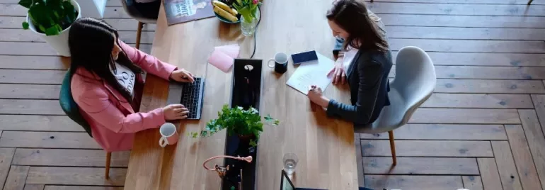 Persone che lavorano a un tavolo con computer portatili e piante.