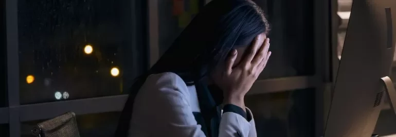 Persona davanti al computer con mani sul viso in un ufficio di notte.