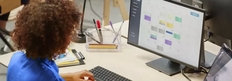 Persona in ufficio al computer controlla un calendario digitale.
