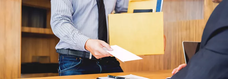 Un dipendente, in giacca e cravatta, consegna una lettera di dimissioni al suo datore di lavoro mentre tiene in mano una scatola con documenti.