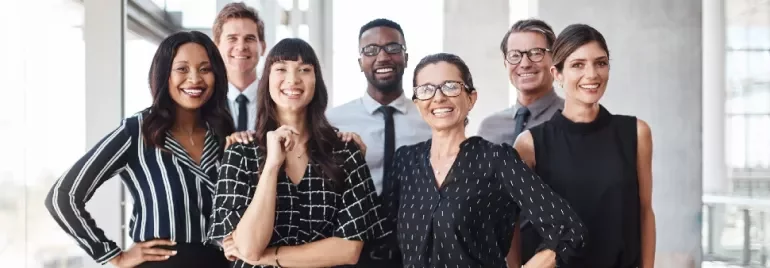Gruppo eterogeneo di adulti in abbigliamento professionale che sorridono in un contesto d’ufficio.