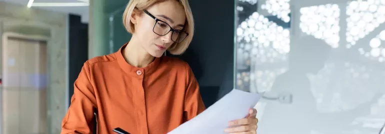 Donna bionda con occhiali che legge un foglio di carta