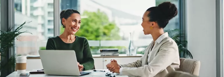 Due professioniste discutono ad un tavolo, di fronte ad un laptop