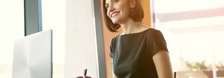 Persona sorridente seduta al tavolo con laptop aperto.