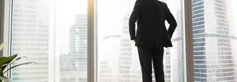 Persona in abito guarda fuori dalla finestra di un grattacielo.