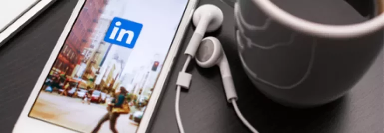 Smartphone con app LinkedIn aperta su scrivania accanto a tazza di caffè.