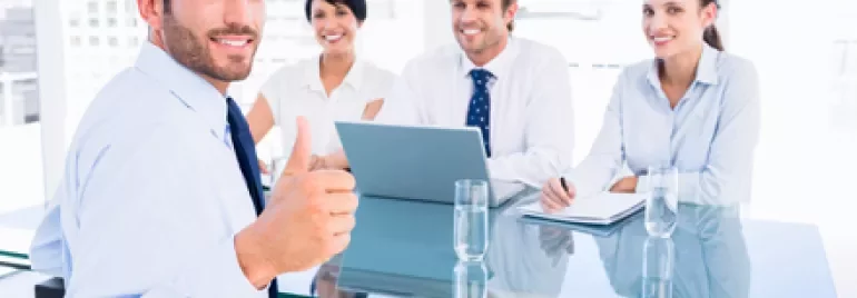 Persone in riunione sorridono intorno a un tavolo di vetro.
