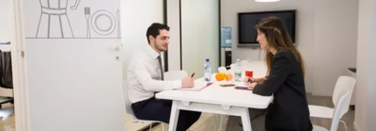 Due persone in riunione sedute a un tavolo bianco in ufficio moderno.