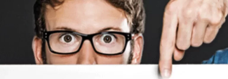 Persona con occhiali guarda sopra un cartello bianco.